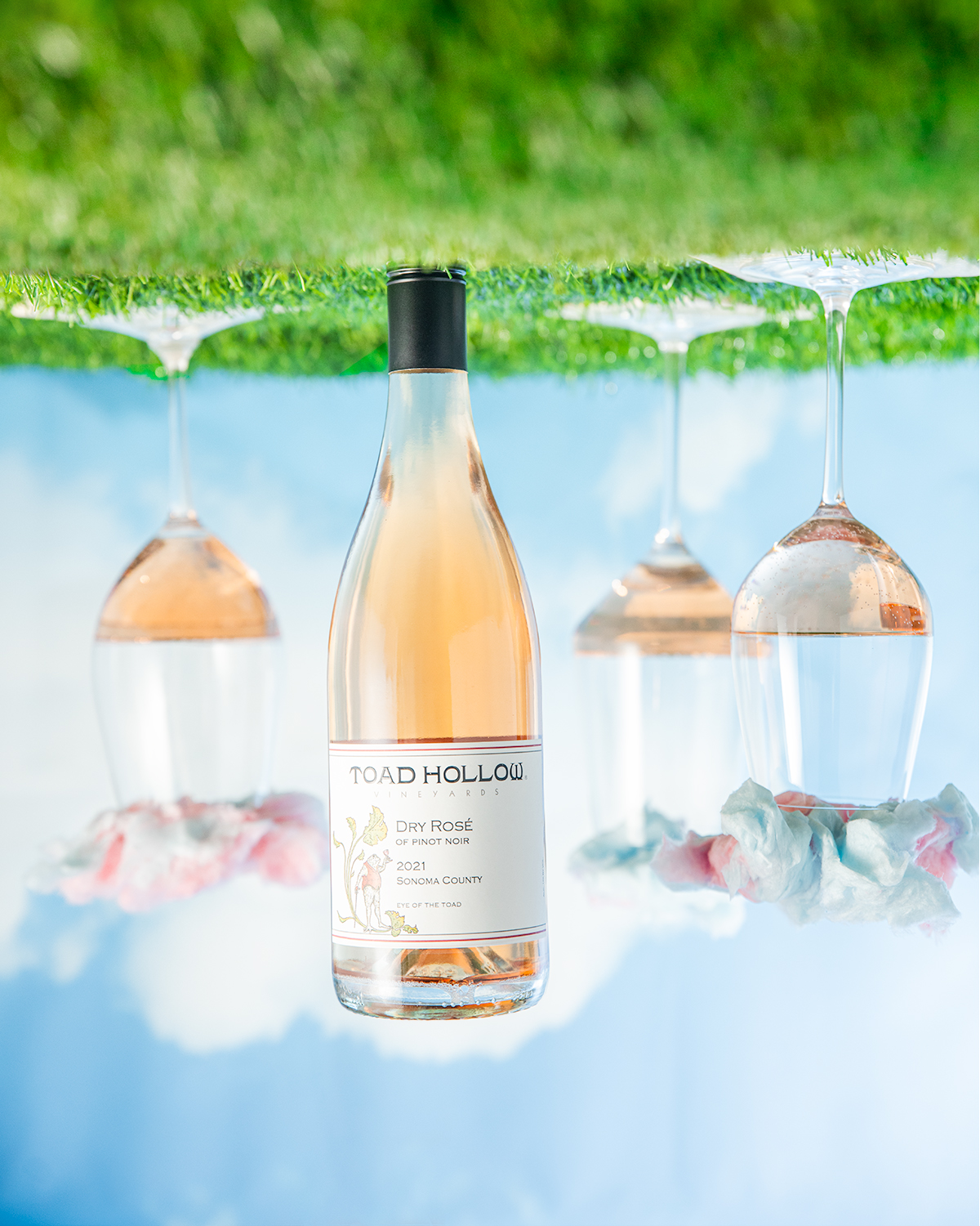 A bottle of rose wine, the grass is at the top and the sky is at the bottom