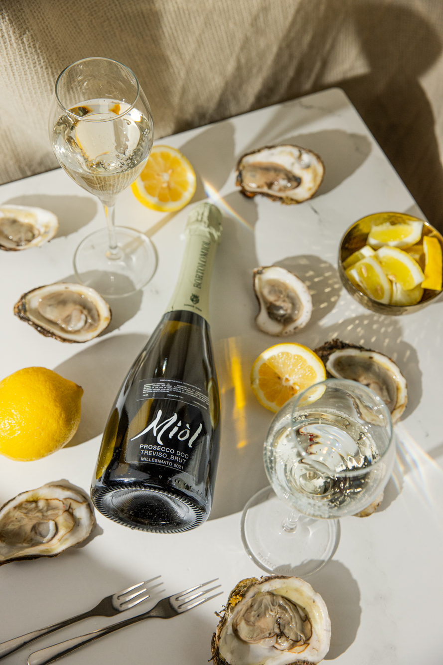 A bottle of prosecco surrounded by oysters, long shadows