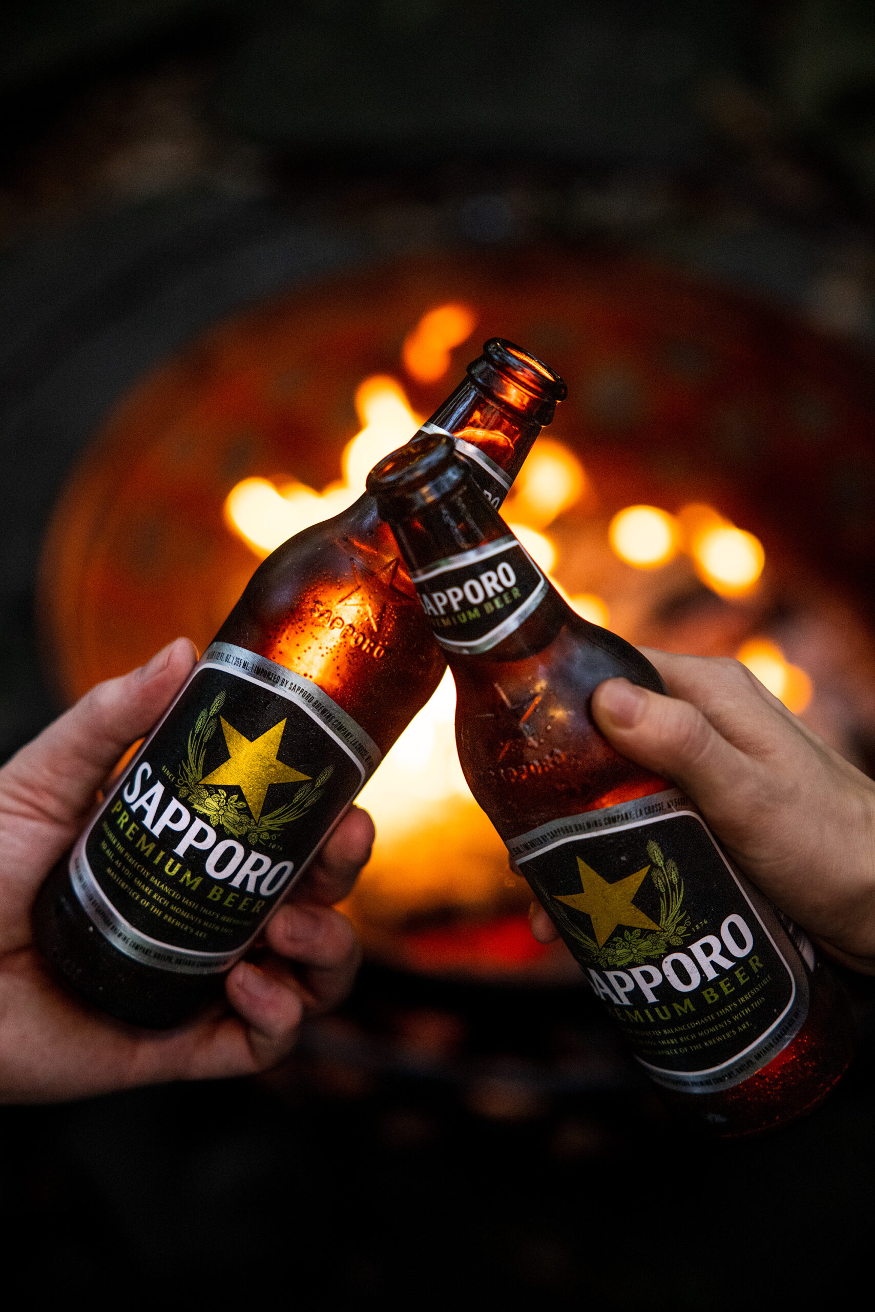 Two Sapporo bottles Cheers in front of a fire pit